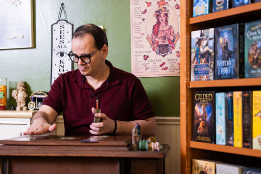 A Gentleman Siting at a Table, Bookshelf to his left filled with Tarot Decks